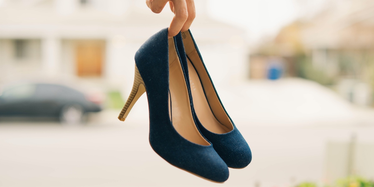 Two fingers holding onto blue heels in front of a blurred background